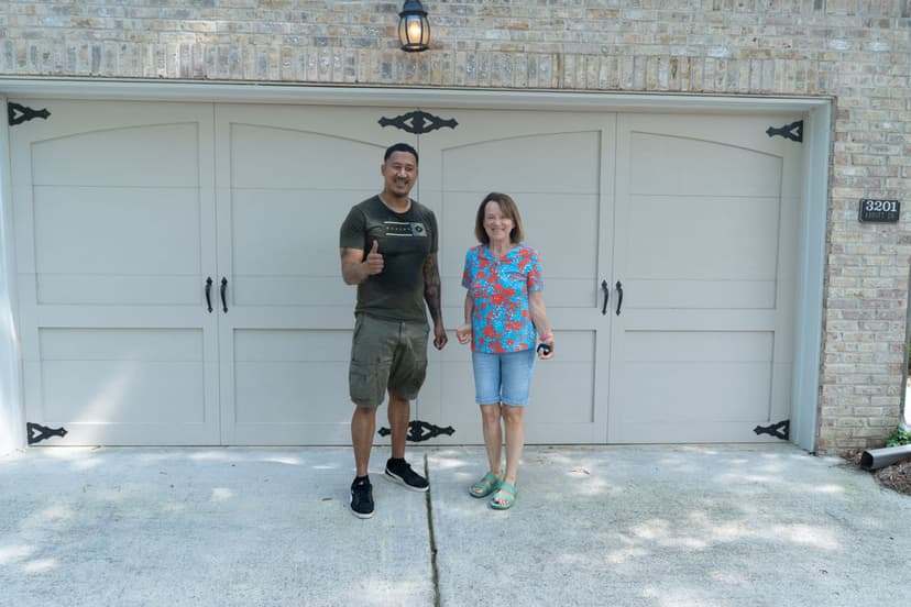Man and woman posing together in front of a garage door, smiling and giving a thumbs up.